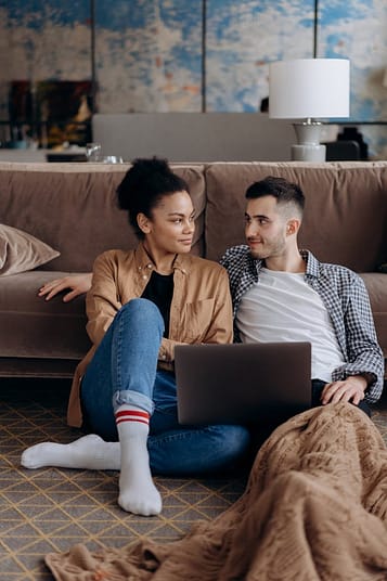 pexels-photo-6894032 Couple sitting on floor with laptop, sharing a warm and cozy moment.
